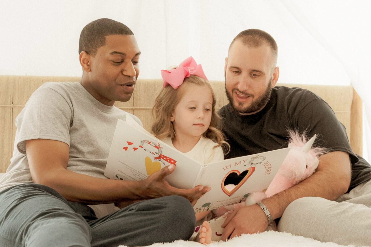 Deux papas lisent un livre à leur enfant.