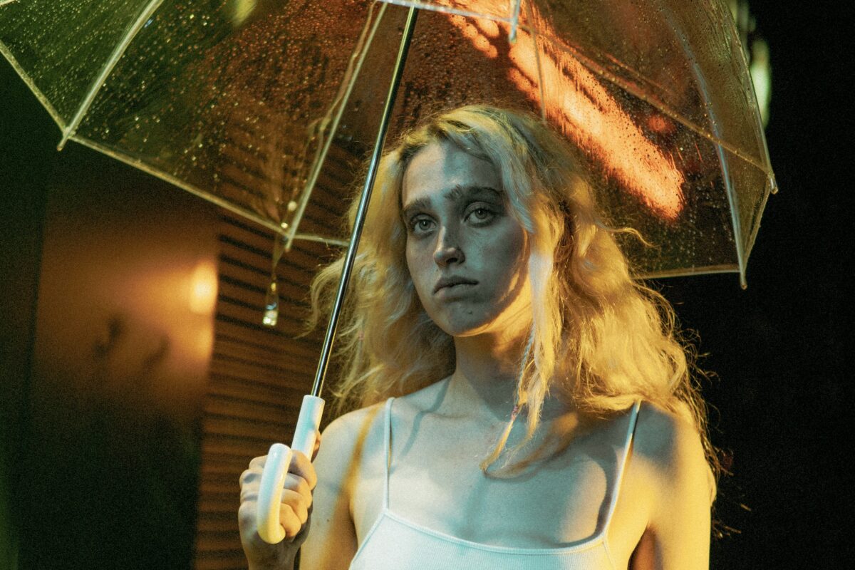 Une personne blonde est dehors, elle tient un parapluie. C'est la nuit.