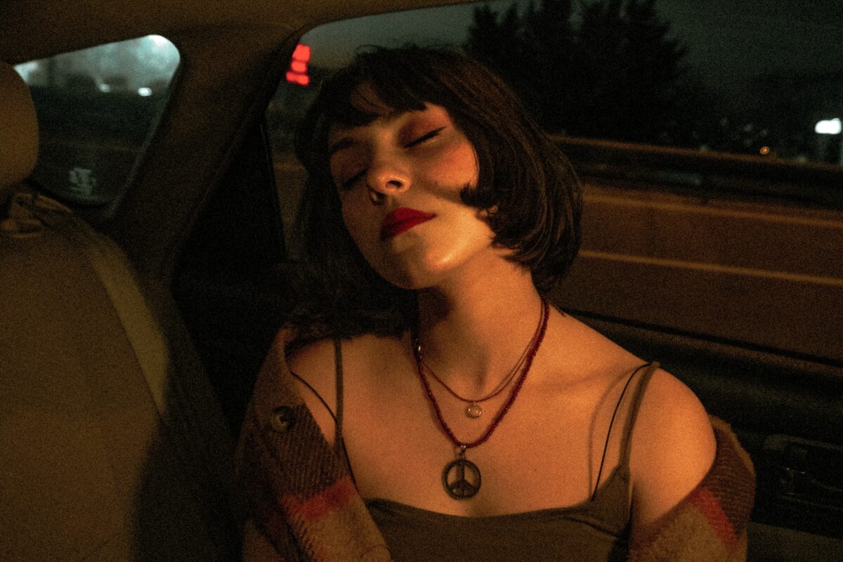 Personne assise sur la banquette arrière d'une voiture. Elle a les yeux fermés et la tête penchée vers l'arrière.