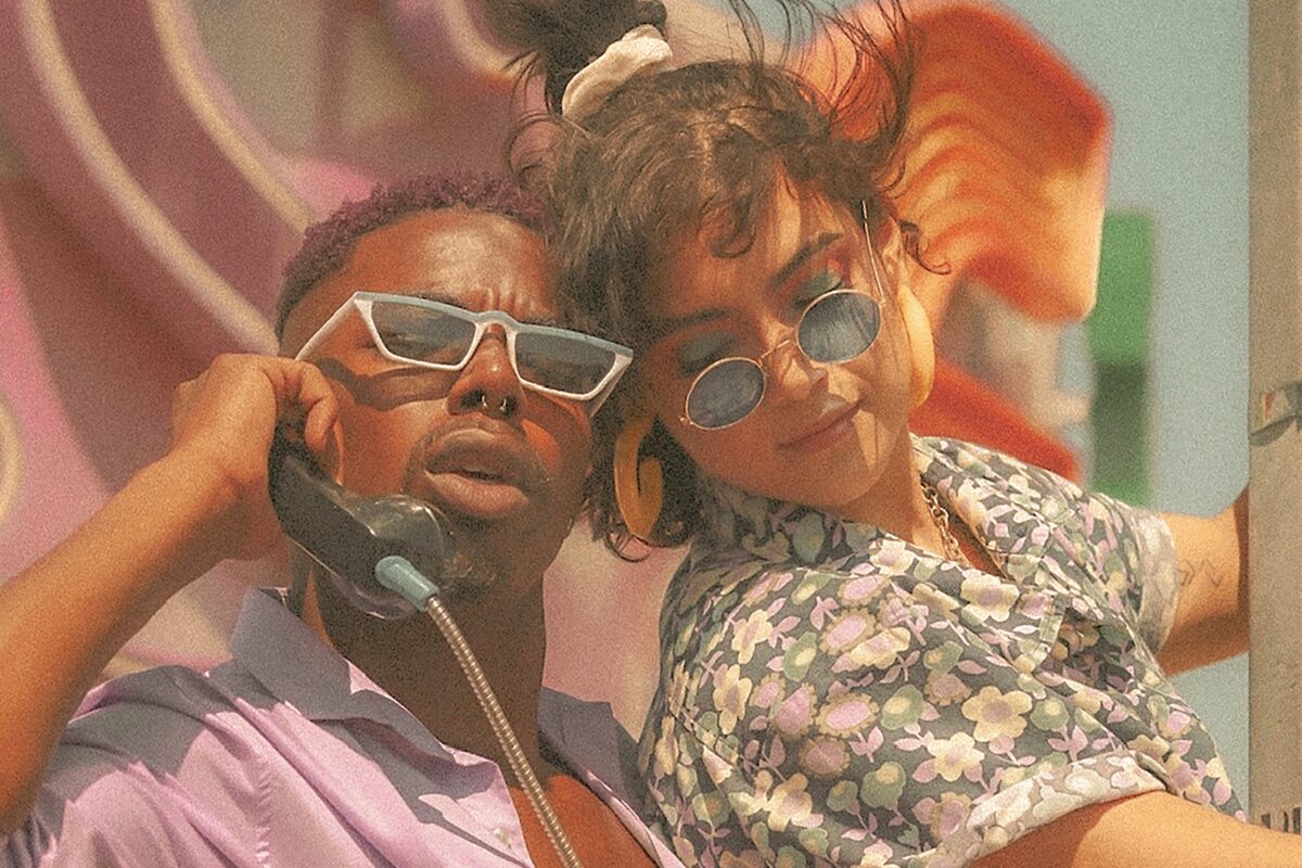Deux personnes sont dehors. Elles portent des lunettes de soleil et l'une d'elle est au téléphone.