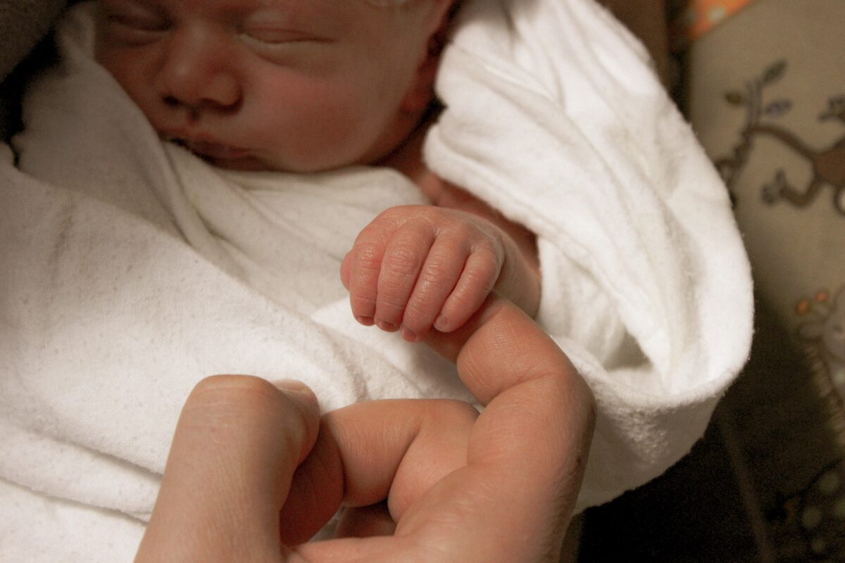 Un bébé naissant tient un doigt d'adulte.