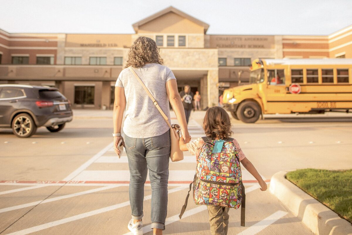 Un parent tient la main de son enfant. Ils marchent vers une école.